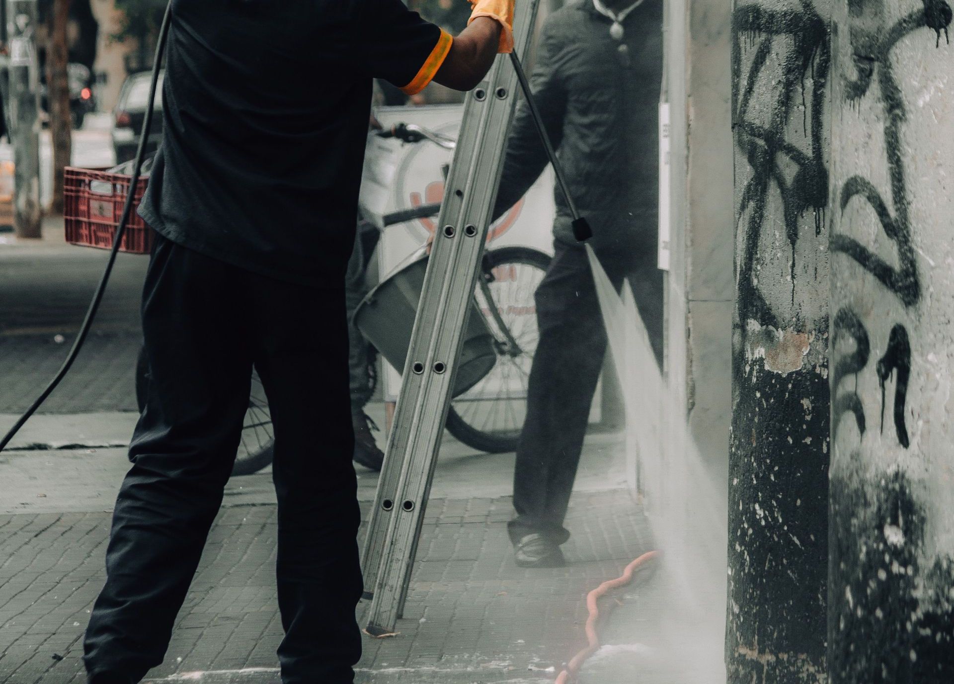 Workers cleaning graffiti off city building facade with a pressure hose.